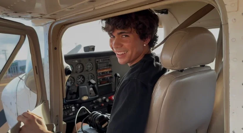 Aiden smiling back toward the camera from the pilot’s seat, with the aircraft instrument panel in view.